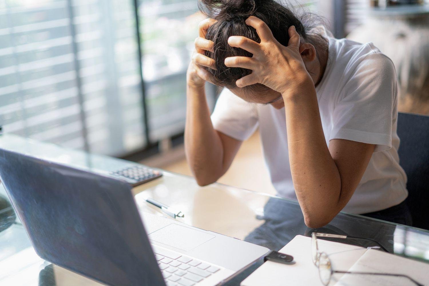 A woman looking overwhelmed and distressed, holding her head in her hands.